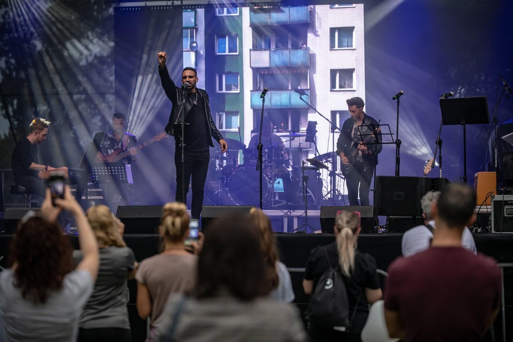 Sami Harb performing on an open-air stage with a live band, the audience filming